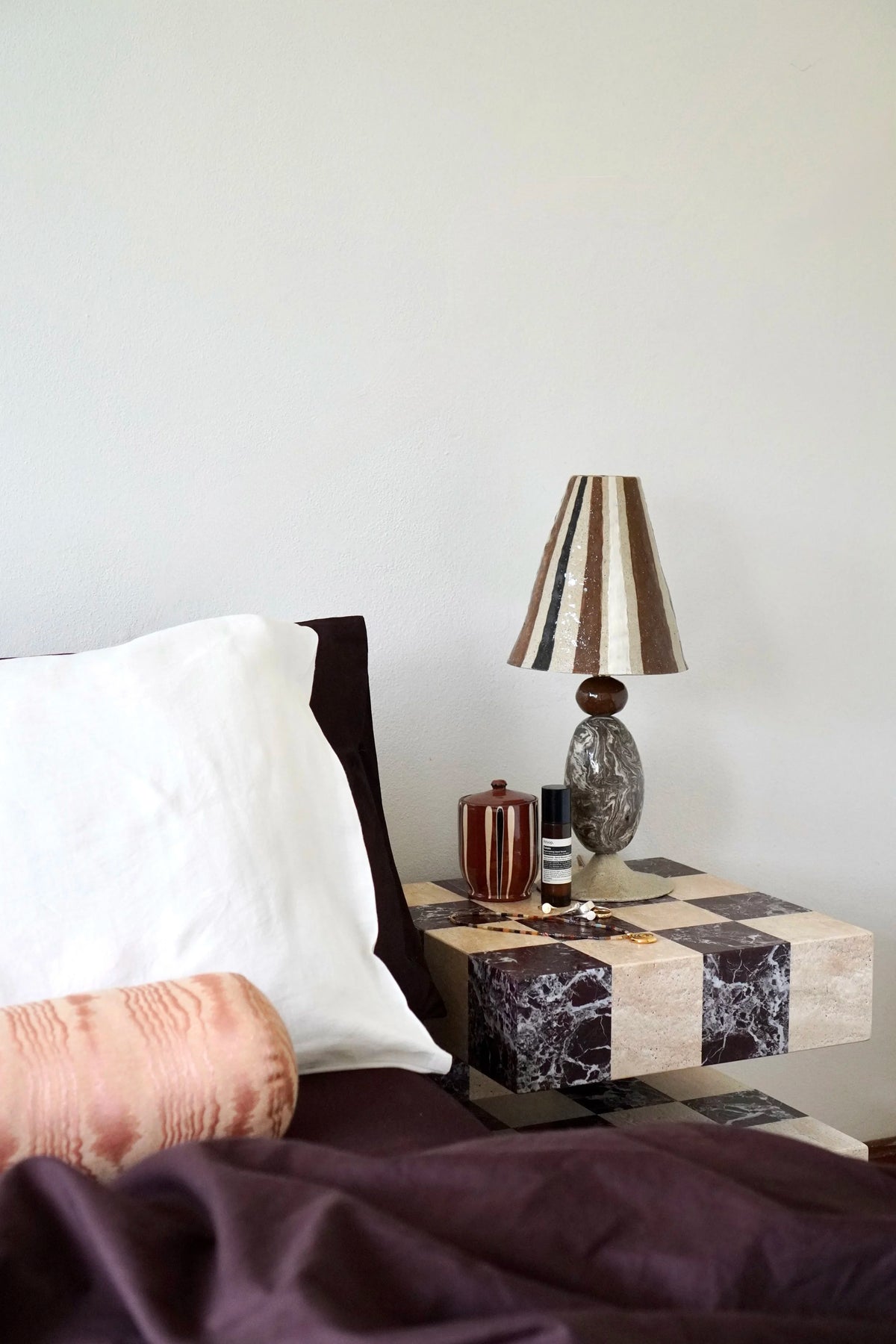 Stevie Table Lamp by Tantri Mustika on a bedside table: a striped shade in brown, cream and grey over a marbled base