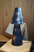 Merlin Table Lamp by Tantri Mustika, deep navy stoneware with platinum lustre stars, on a woven stool
