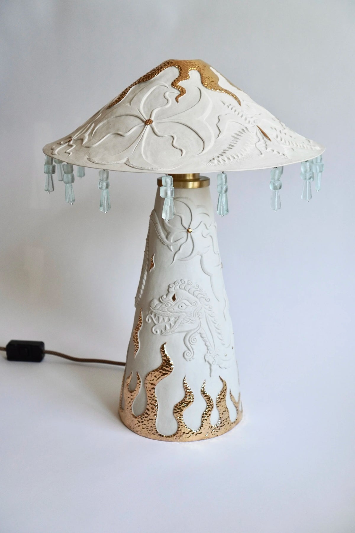 Ukiran Table Lamp by Tantri Mustika: carved white stoneware with gold lustre flames around the base and a glass bead fringe on the shade