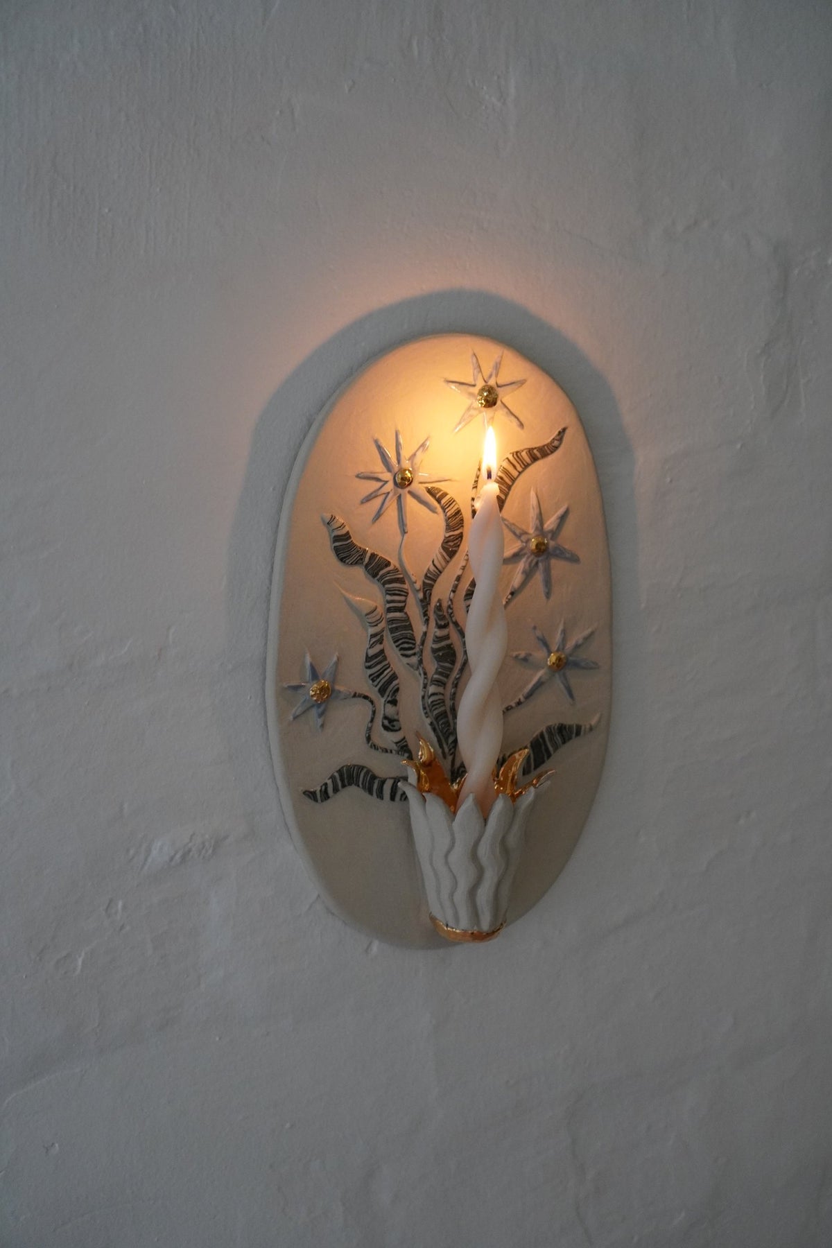 Oval candle sconce by Tantri Mustika with star flowers and gold lustre, lit, Flame 2024