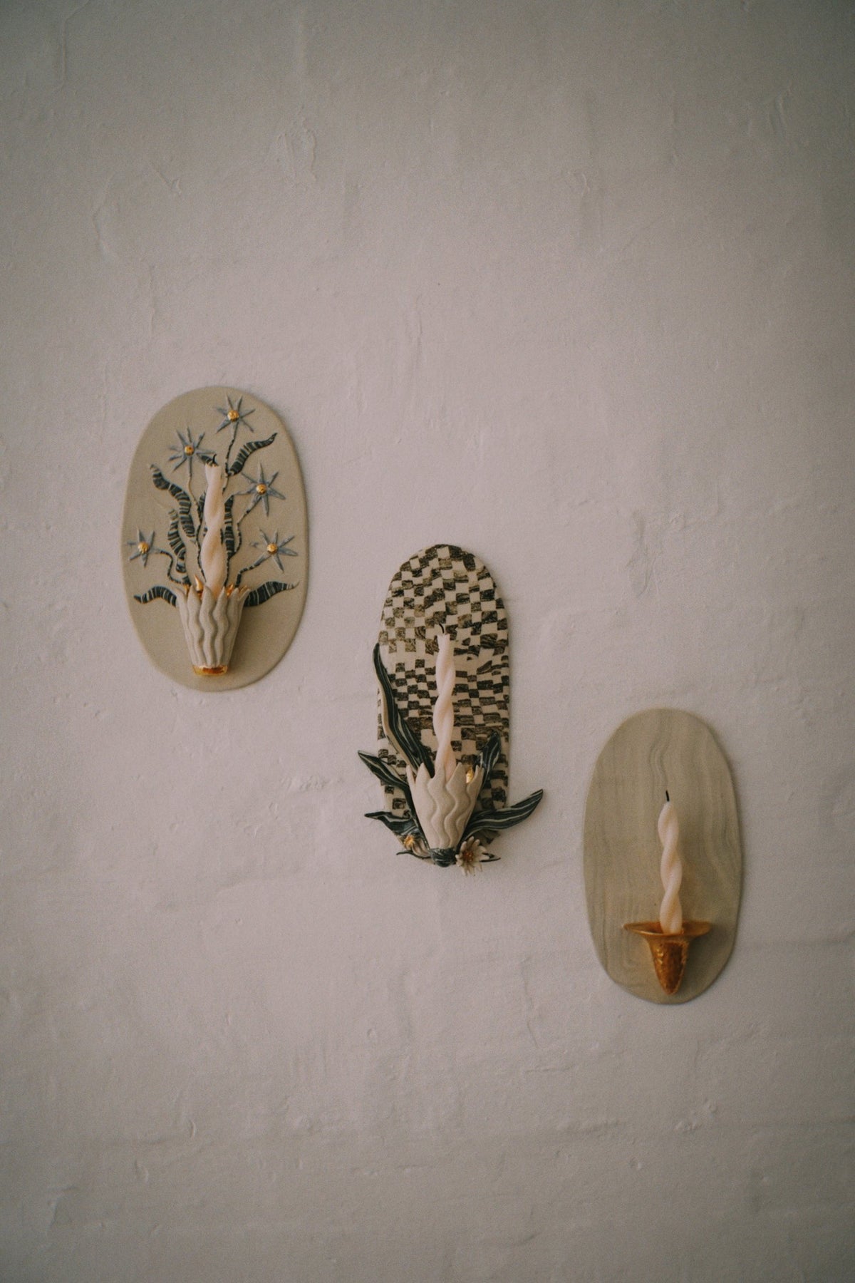 Three candle sconces by Tantri Mustika on a white brick wall: star flowers, checkered and plain, Flame 2024
