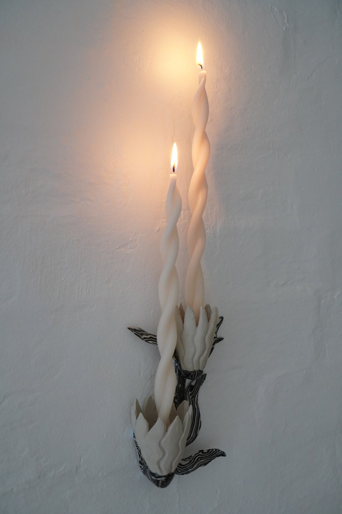 Unfurled candle sconce by Tantri Mustika with two twisted candles, lit, Flame 2024