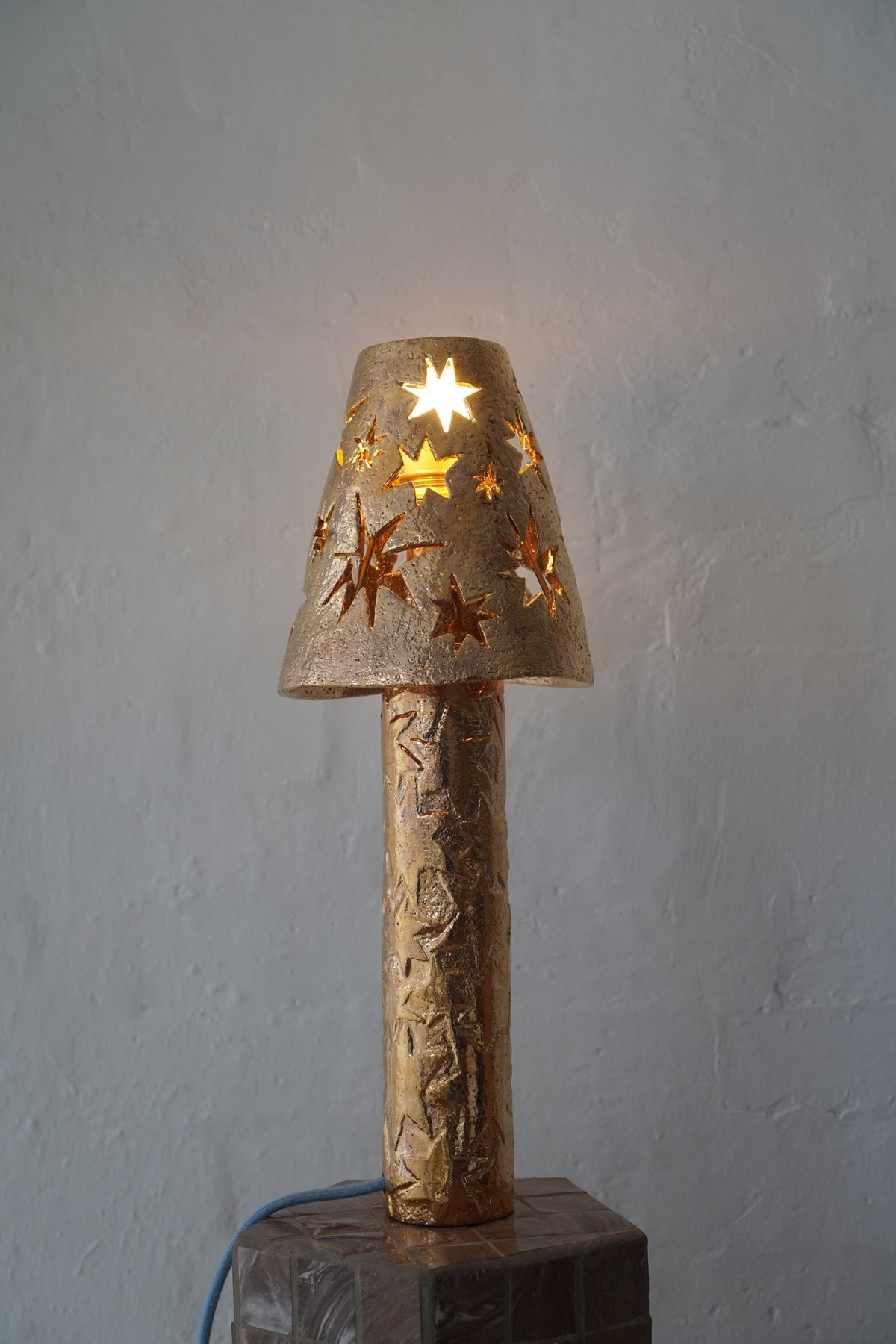 “She’s going to be very bright”, a gold lustre ceramic lamp by Tantri Mustika with star cut-outs, lit, 2024