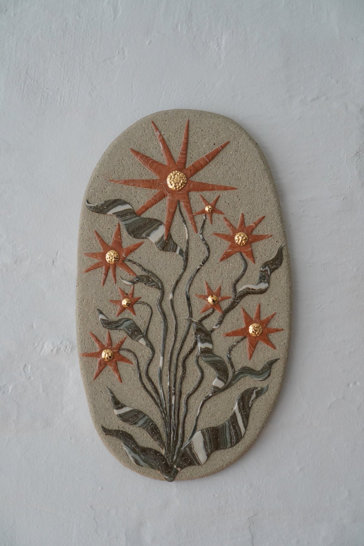 “The time will come and you will bloom”, an oval stoneware wall piece by Tantri Mustika with orange star flowers, 2024