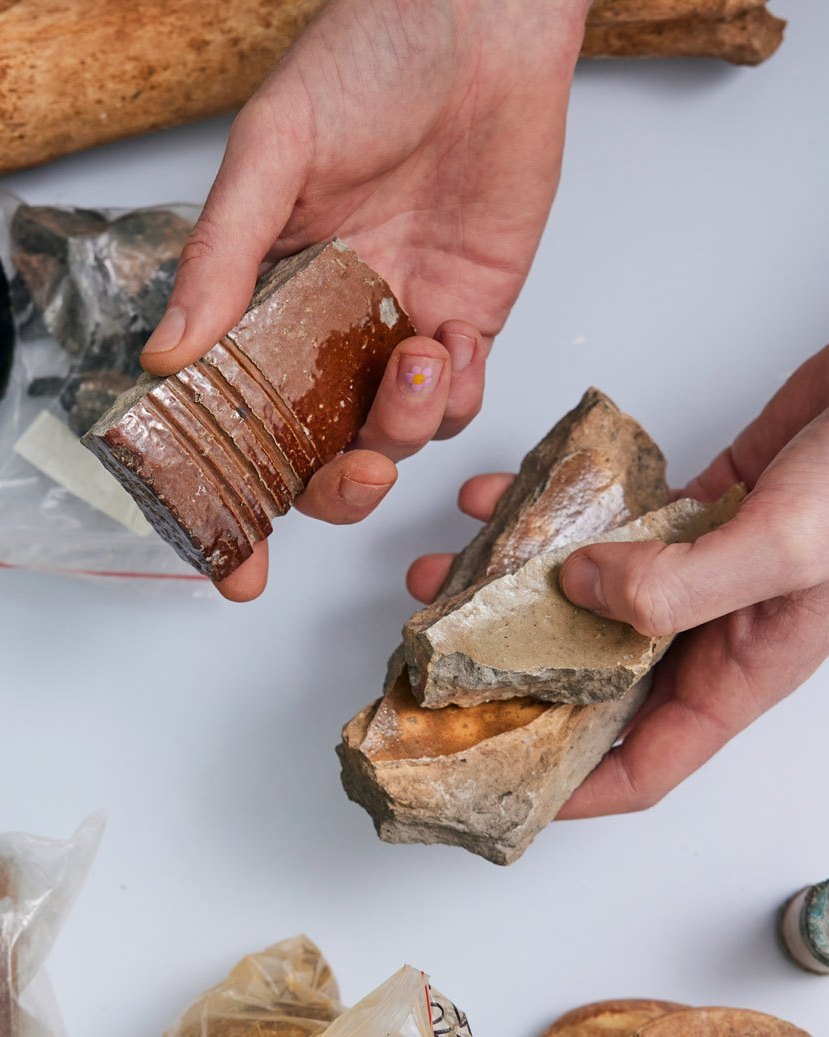 Hands holding glazed ceramic fragments from the Metro Tunnel dig sites, Unearthed 2022